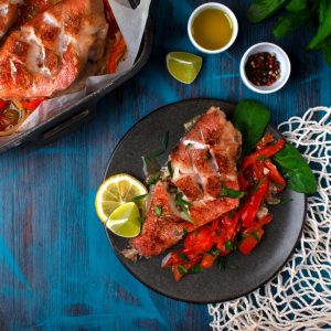 Baked redfish or perch with vegetables served on the plate on the blue table. Healthy fish dish.