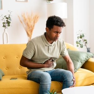 Black man sitting on sofa. stomach pain