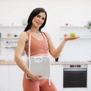 Health coach with measuring tape, scales and apple at home