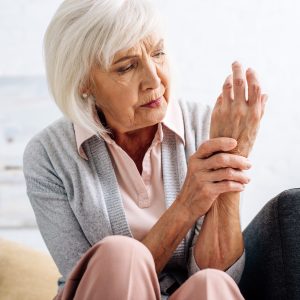 senior woman having hand Arthritis and sitting on sofa in apartment
